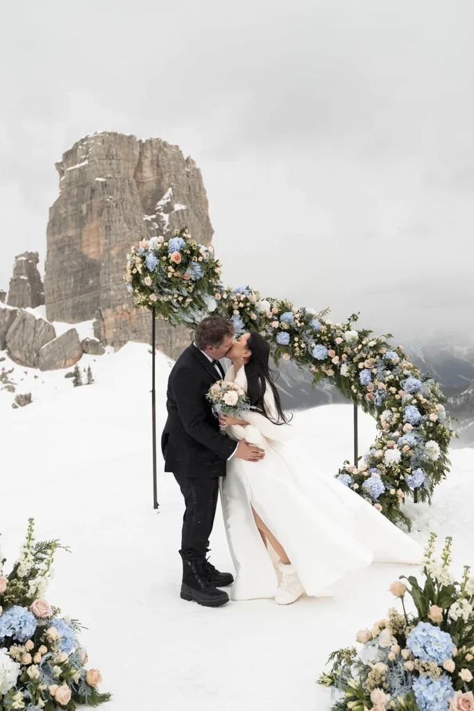 Tracy and Ryan kissing beneath a floral arch at the Cinque Torri in winter